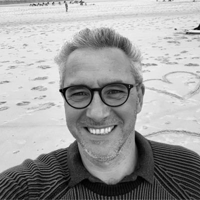 Portrait en noir et blanc de Déniz Bayirli, souriant, lunettes rondes