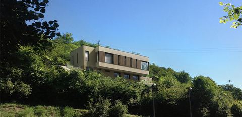 La maison vue de loin, posée à mi-pente dans la végétation